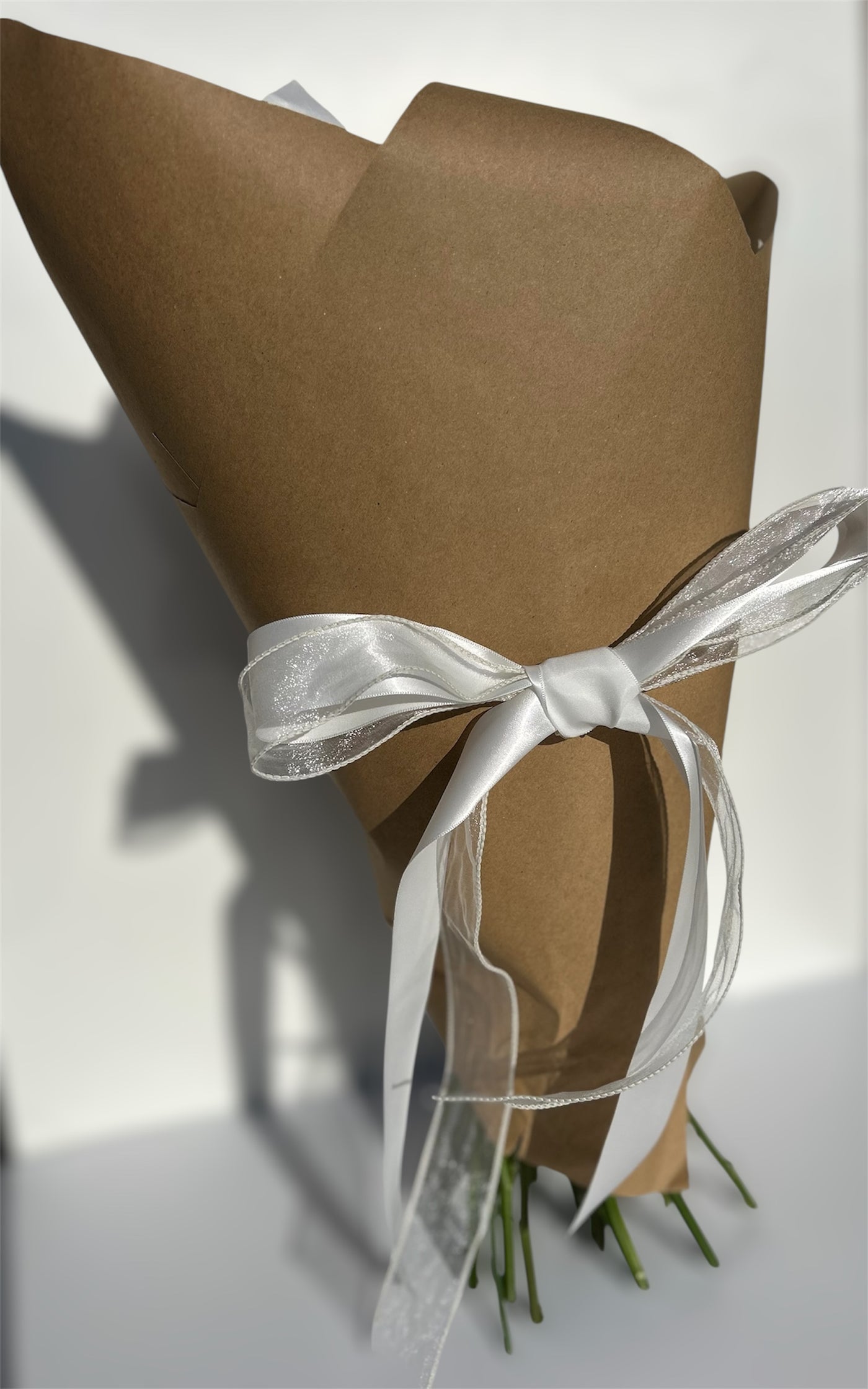 Bouquet of flowers wrapped in brown paper with a white ribbon on a light background