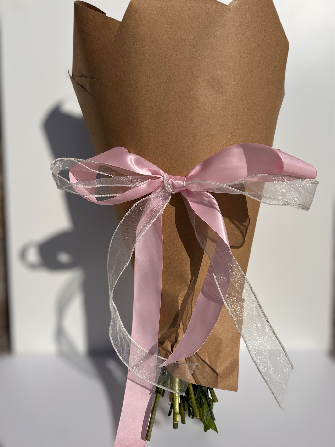 Bouquet wrapped in brown paper with a pink ribbon on a white background
