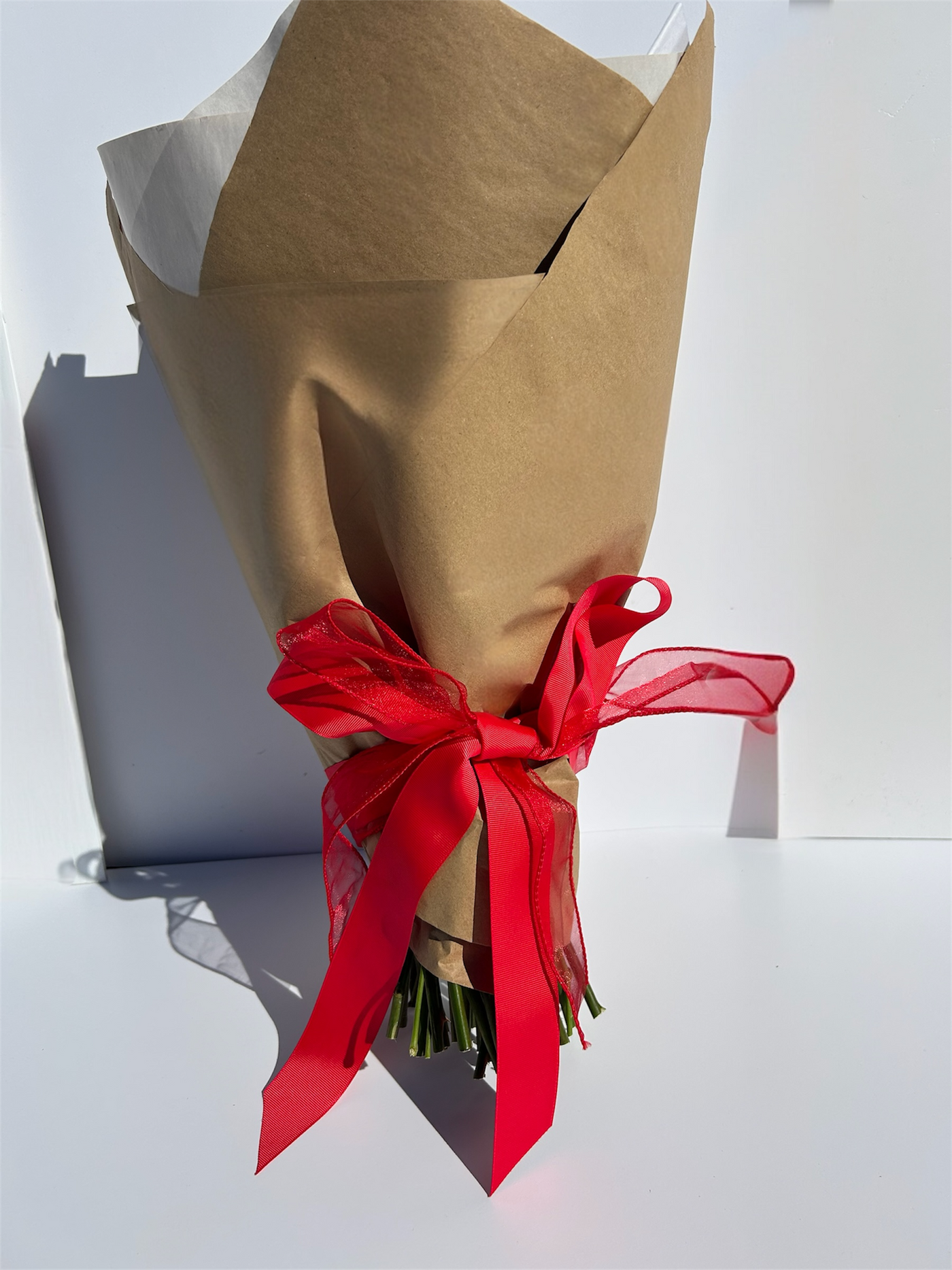 Bouquet wrapped in brown paper with a red ribbon on a white background