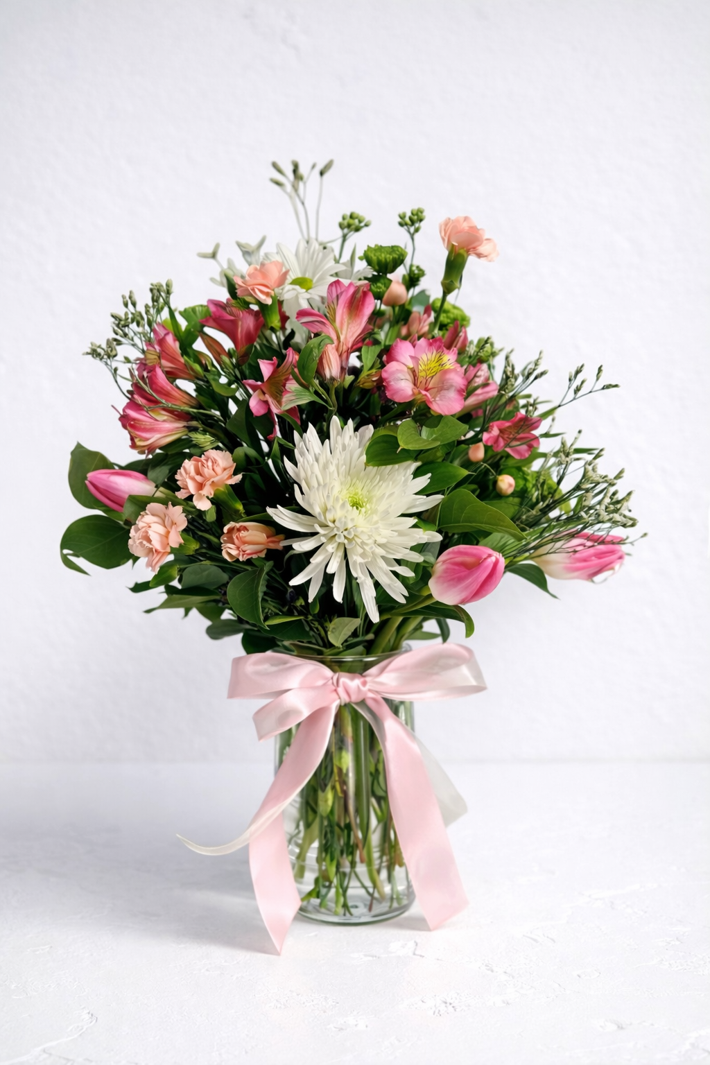 Bouquet of flowers with a pink ribbon in a clear vase on a white background